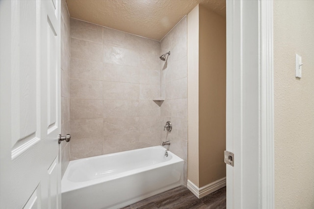 bathroom with a textured ceiling, baseboards, shower / bathing tub combination, and wood finished floors