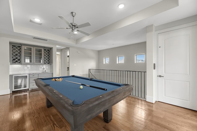 game room with visible vents, wood finished floors, indoor wet bar, wine cooler, and a tray ceiling