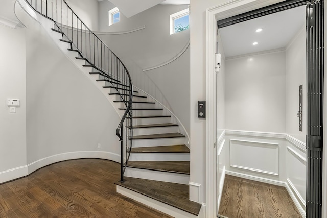 stairway with a high ceiling, elevator, and wood finished floors