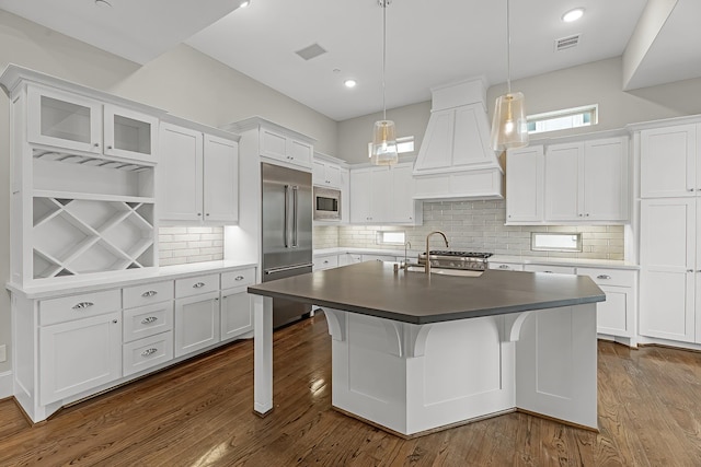 kitchen with built in appliances, white cabinets, custom range hood, and visible vents