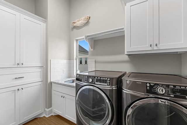 washroom with a sink, cabinet space, wood finished floors, and washer and dryer
