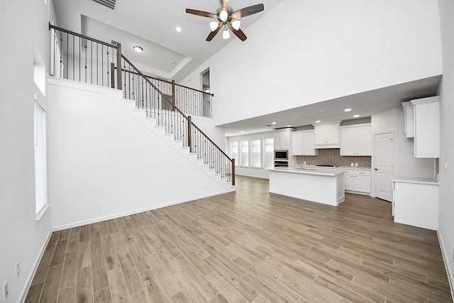 4166 Colony Ln, Missouri City, TX 77459 - unfurnished living room with a towering ceiling, ceiling fan, light wood finished floors, a sink, and stairs