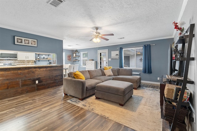 living room featuring visible vents, ornamental molding, wood finished floors, ceiling fan, and a textured ceiling
