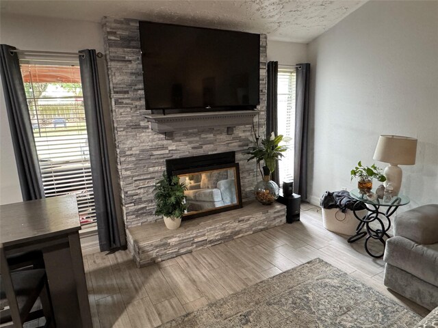 living room featuring a textured ceiling, a stone fireplace, a wealth of natural light, and wood finished floors