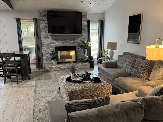 living area with a healthy amount of sunlight, a textured ceiling, a stone fireplace, and wood finished floors