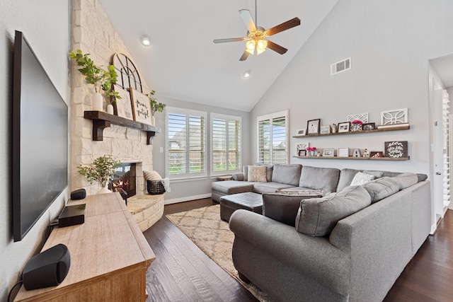 living room featuring visible vents, a stone fireplace, dark wood-style floors, high vaulted ceiling, and a ceiling fan