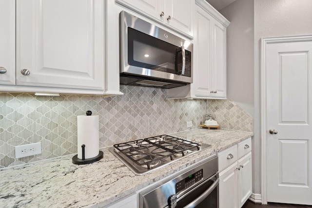 kitchen with appliances with stainless steel finishes, decorative backsplash, light stone countertops, and white cabinetry