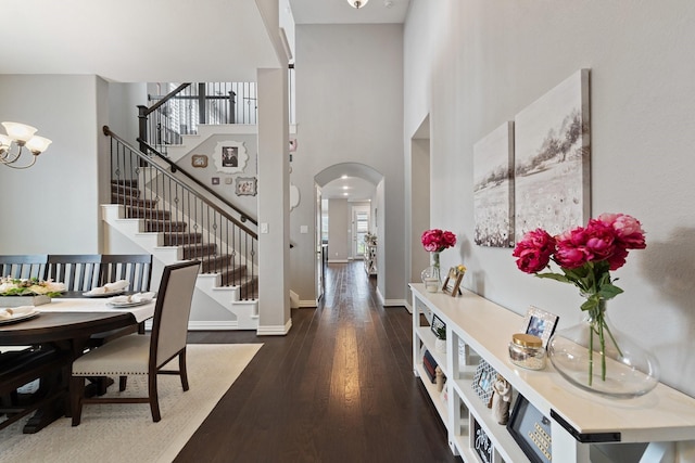 entrance foyer featuring a high ceiling, arched walkways, baseboards, wood finished floors, and stairway