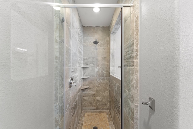 bathroom with a textured wall and a tile shower