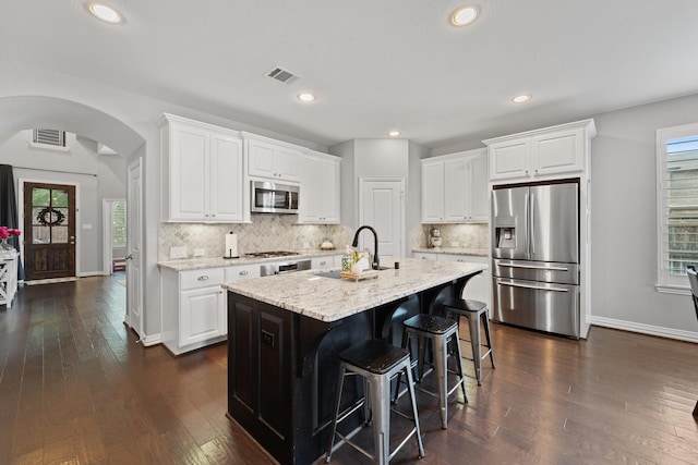 kitchen featuring visible vents, arched walkways, a sink, white cabinets, and stainless steel appliances
