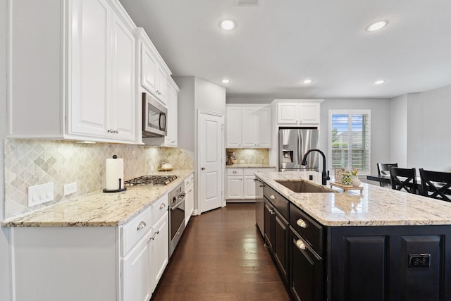 kitchen with a center island with sink, dark wood-type flooring, white cabinets, a sink, and appliances with stainless steel finishes