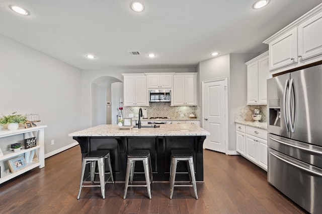 kitchen featuring stainless steel appliances, arched walkways, white cabinetry, and a sink
