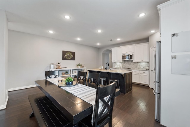 dining space featuring recessed lighting, arched walkways, dark wood-style flooring, and baseboards