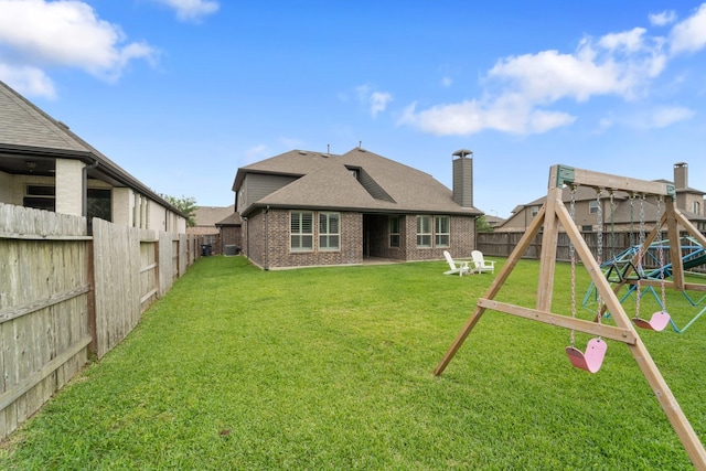 rear view of house with a playground, a lawn, a fenced backyard, and brick siding