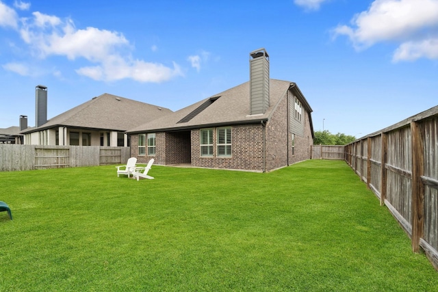 rear view of property with a chimney, roof with shingles, a lawn, brick siding, and a fenced backyard