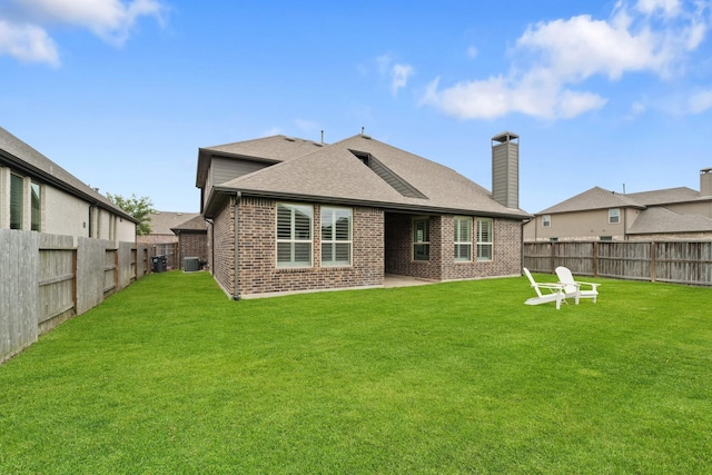 back of property featuring a lawn, brick siding, a fenced backyard, and roof with shingles