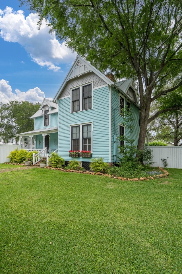victorian house featuring a porch, fence, and a front yard
