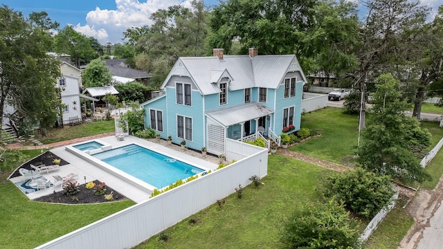 back of house with a chimney, metal roof, a pool with connected hot tub, a fenced backyard, and a yard