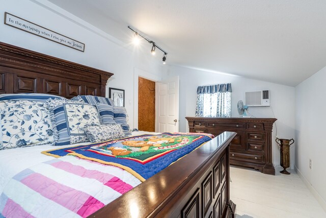 bedroom featuring rail lighting, baseboards, lofted ceiling, and a wall mounted air conditioner