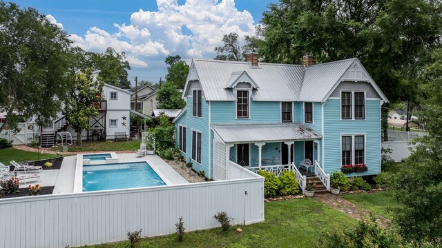 rear view of house with metal roof, a chimney, fence private yard, an outdoor pool, and stairs