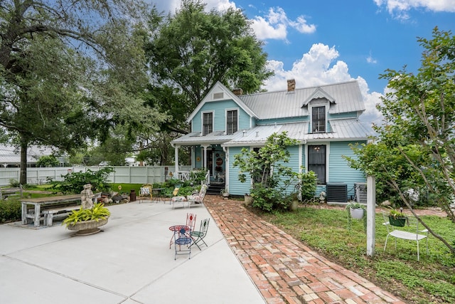 view of front of home with a patio, fence, a chimney, and metal roof