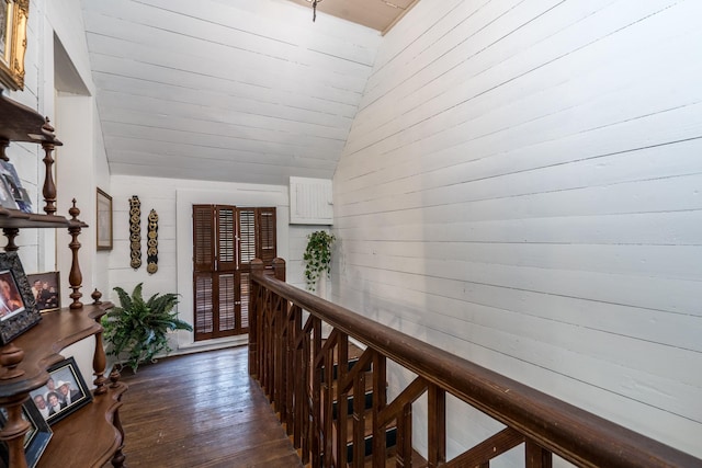 corridor featuring wood walls, dark wood-style flooring, lofted ceiling, and an upstairs landing