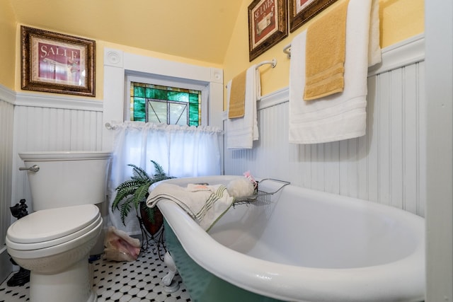 full bath featuring toilet, a freestanding bath, and a wainscoted wall