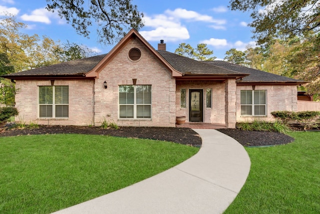 ranch-style house featuring brick siding, roof with shingles, a front yard, and a chimney