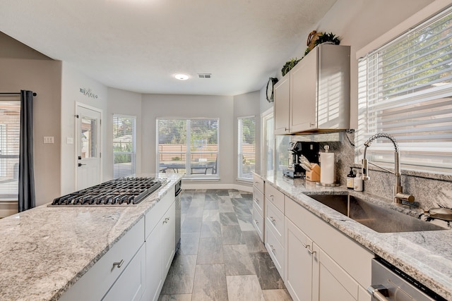 kitchen featuring appliances with stainless steel finishes, a sink, stone finish flooring, backsplash, and visible vents