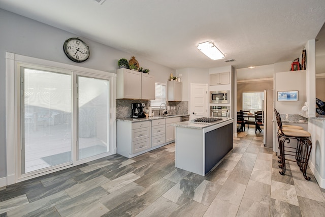 kitchen featuring a center island, light stone counters, a sink, appliances with stainless steel finishes, and backsplash