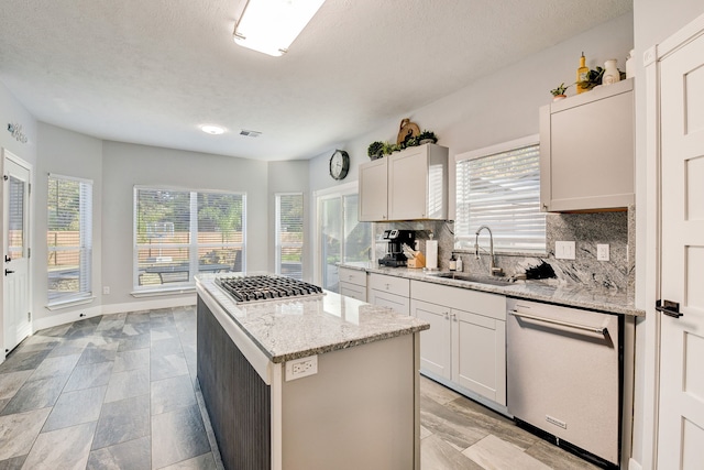 kitchen with a center island, tasteful backsplash, light stone counters, a sink, and stainless steel appliances