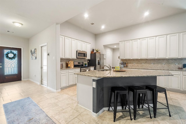 kitchen featuring decorative backsplash, a kitchen island with sink, a breakfast bar area, a sink, and stainless steel appliances