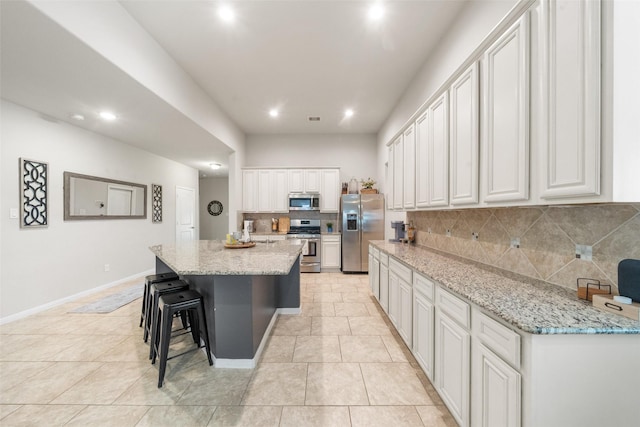 kitchen with white cabinets, light stone countertops, appliances with stainless steel finishes, an island with sink, and tasteful backsplash
