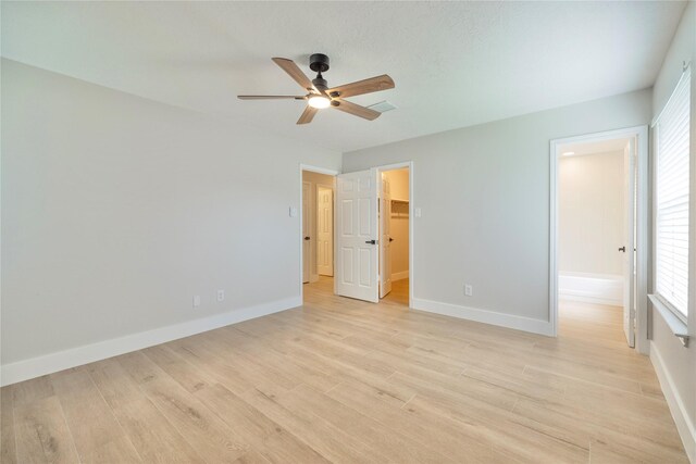 unfurnished bedroom with a ceiling fan, baseboards, a spacious closet, and light wood-style flooring