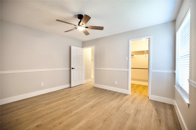 unfurnished bedroom with light wood-style floors, baseboards, multiple windows, and a spacious closet