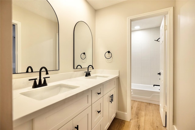full bathroom with double vanity, baseboards, a sink, and wood finished floors