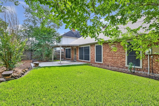 rear view of property featuring brick siding, a patio, a yard, and fence