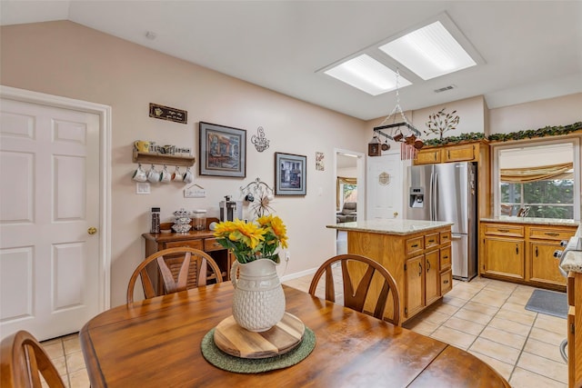 dining space with light tile patterned flooring, visible vents, and vaulted ceiling with skylight