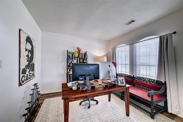 office with baseboards, a textured ceiling, visible vents, and wood finished floors