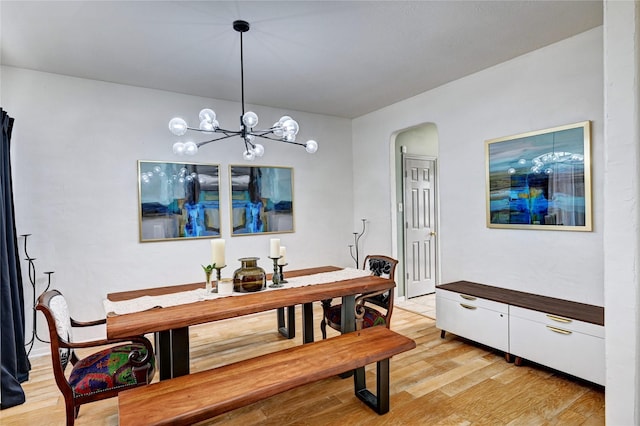 dining room with arched walkways, an inviting chandelier, and light wood-type flooring