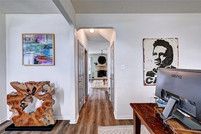 hallway featuring arched walkways, baseboards, and dark wood-style floors