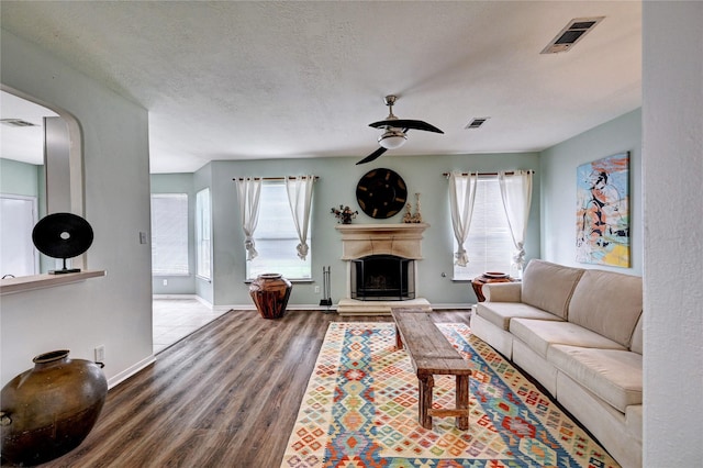 living area with plenty of natural light, ceiling fan, visible vents, wood finished floors, and a fireplace with raised hearth
