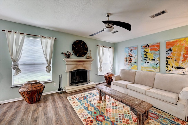 living room with a ceiling fan, visible vents, a fireplace with raised hearth, and wood finished floors