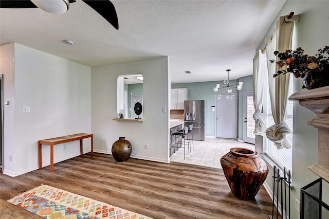 foyer featuring ceiling fan, a textured ceiling, arched walkways, baseboards, and light wood finished floors