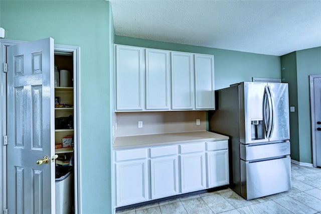 kitchen featuring light countertops, white cabinetry, a textured ceiling, stainless steel fridge with ice dispenser, and light tile patterned floors
