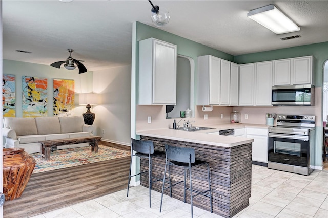 kitchen featuring visible vents, open floor plan, white cabinets, a sink, and appliances with stainless steel finishes