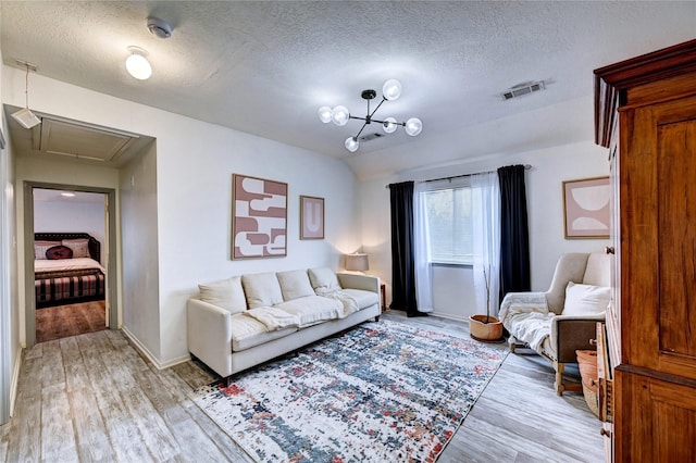 living area featuring attic access, light wood-type flooring, a textured ceiling, and visible vents