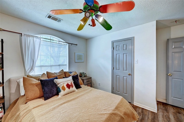 bedroom featuring visible vents, wood finished floors, baseboards, a textured ceiling, and a ceiling fan
