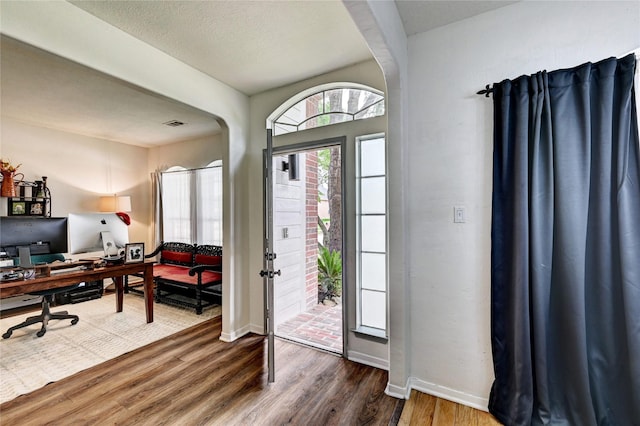 foyer entrance featuring arched walkways, baseboards, and wood finished floors