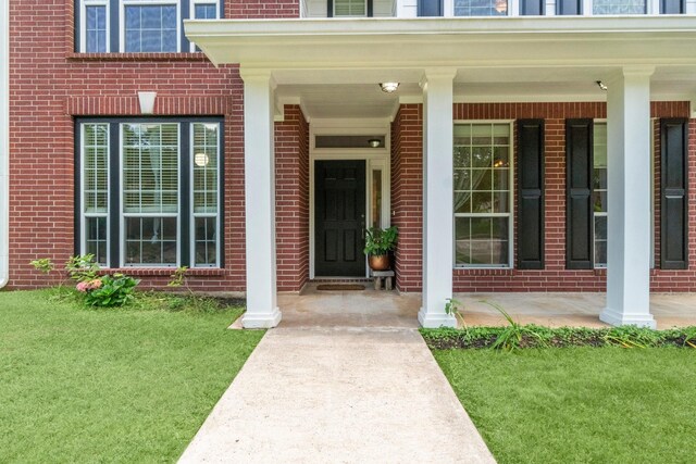 property entrance featuring covered porch, a yard, and brick siding